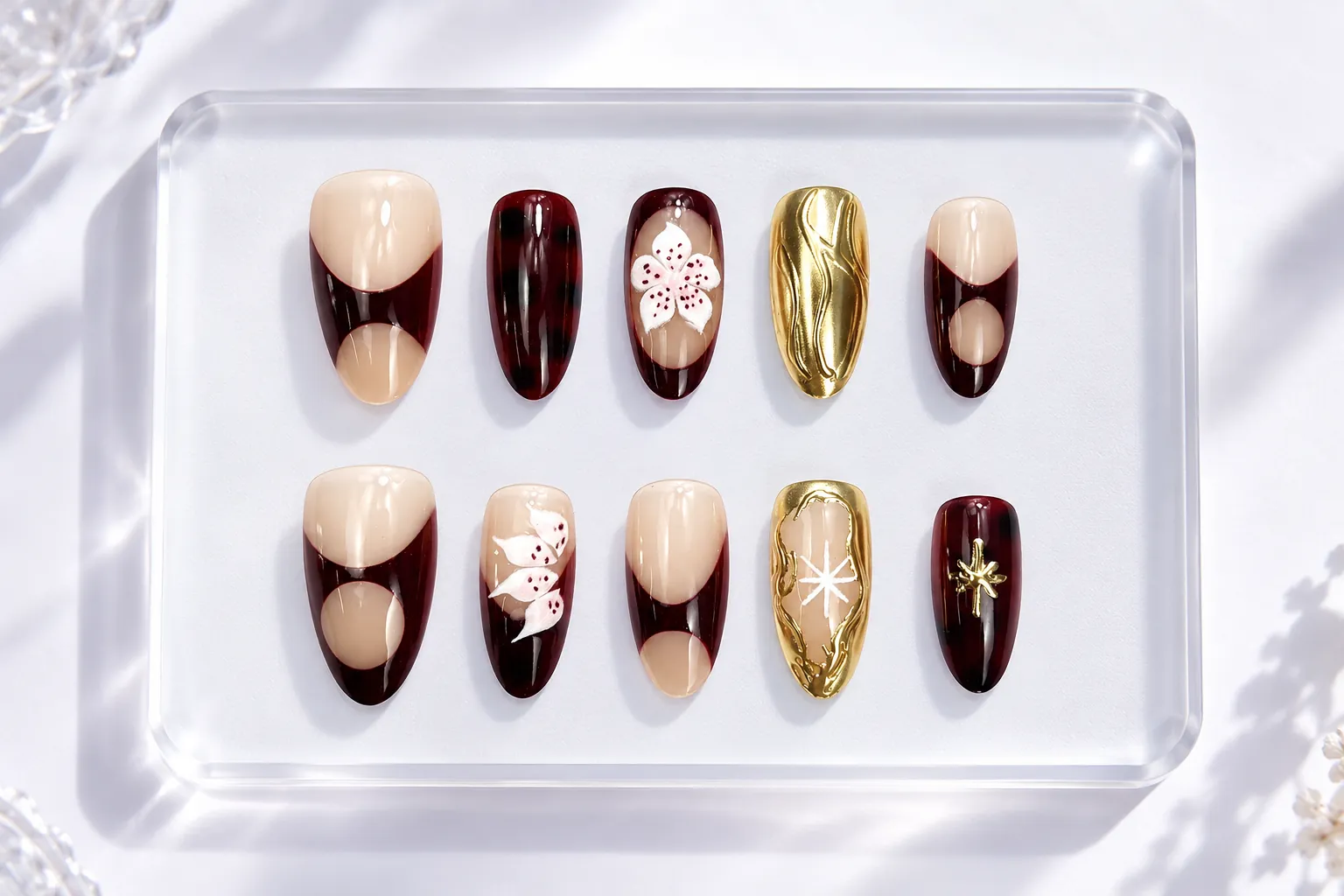 A set of wine red, amber gold and nude almond press-on tips on an acrylic tray